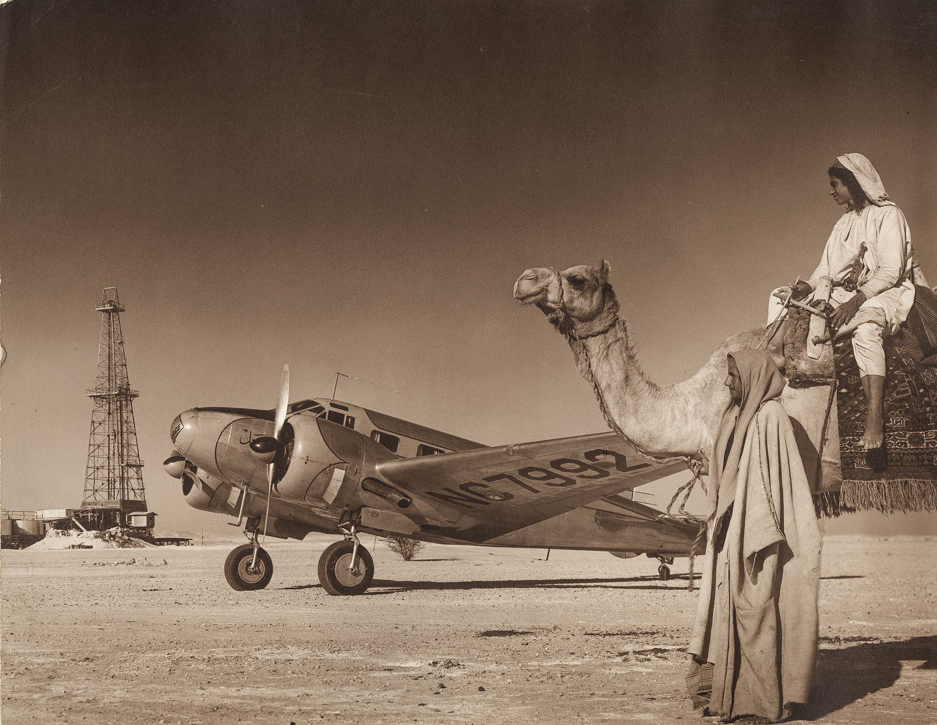 Oil well drilling rig with airplane and men with camel, ARAMCO (SMU Central University Libraries)